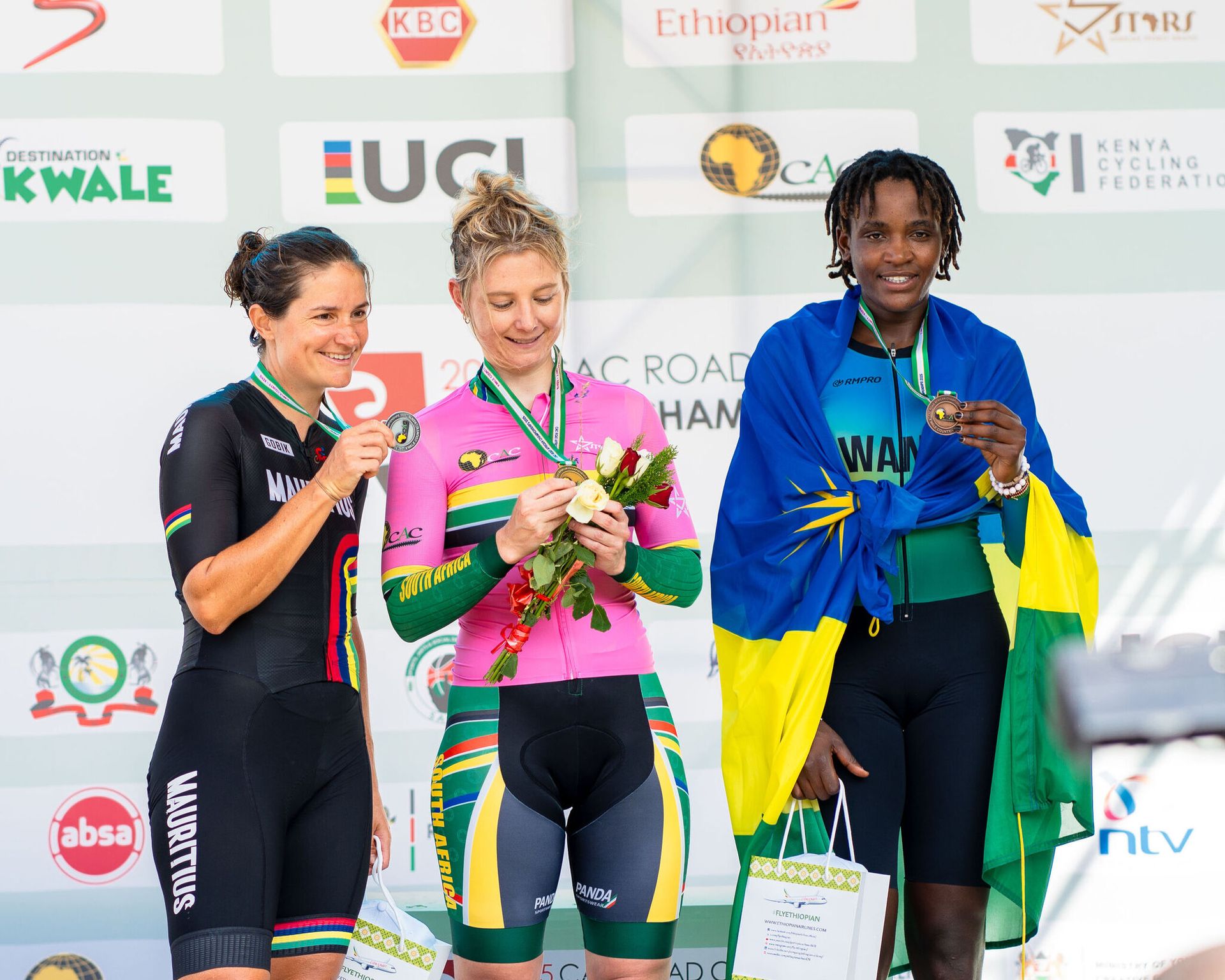 Three riders on the podium, each holding a bouquet