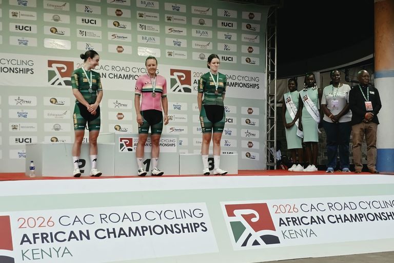 The three South Africans on the podium of the elite women's road race of the 2026 African Road Championships in Kisumu, their medals around their necks, the winner in a pink jersey in the centre; officials and hostesses on the right