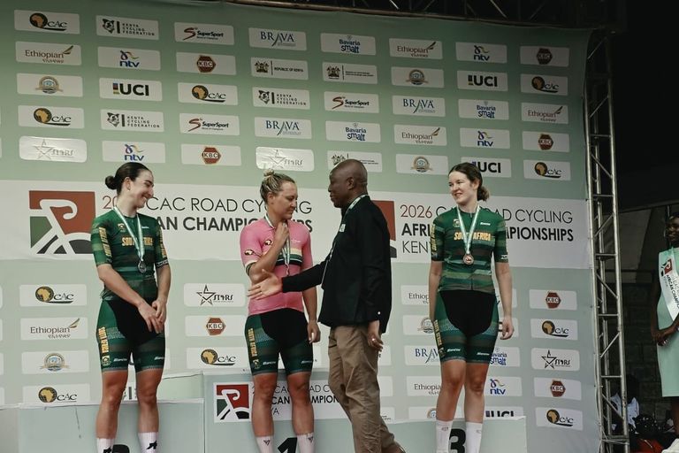 An official shakes hands with the winner in a pink jersey on the top step of the podium, between the second and the third, all in South Africa jerseys