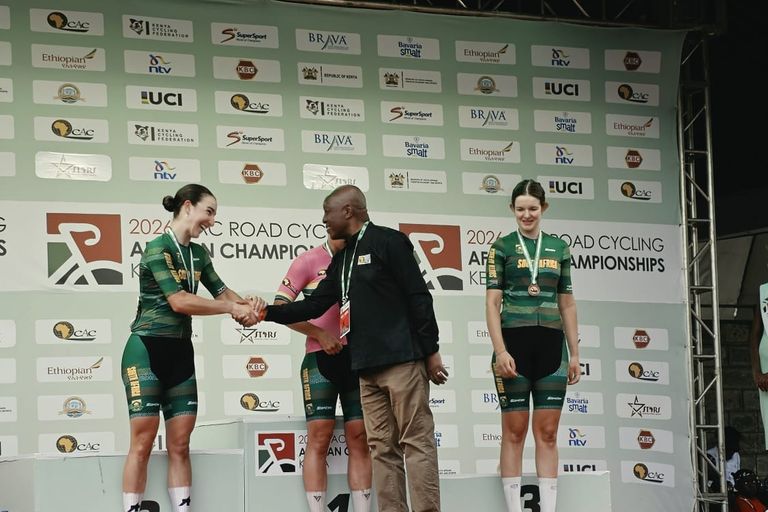 An official shakes hands with the runner-up on her step of the podium, the winner behind him and the third on the right