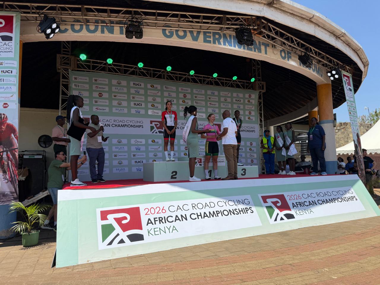 An official presents the winner with her medal on the top step of the 2026 African Road Championships podium in Kisumu, between the second and the third