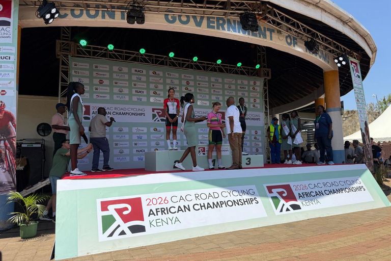 An official congratulates the winner on the top step of the 2026 African Road Championships podium in Kisumu, in front of the partners' boards
