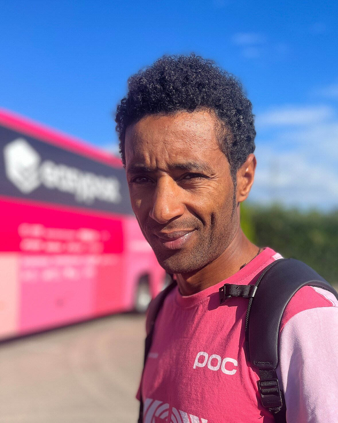 Portrait de Merhawi Kudus en tee-shirt rose, devant le bus de son équipe