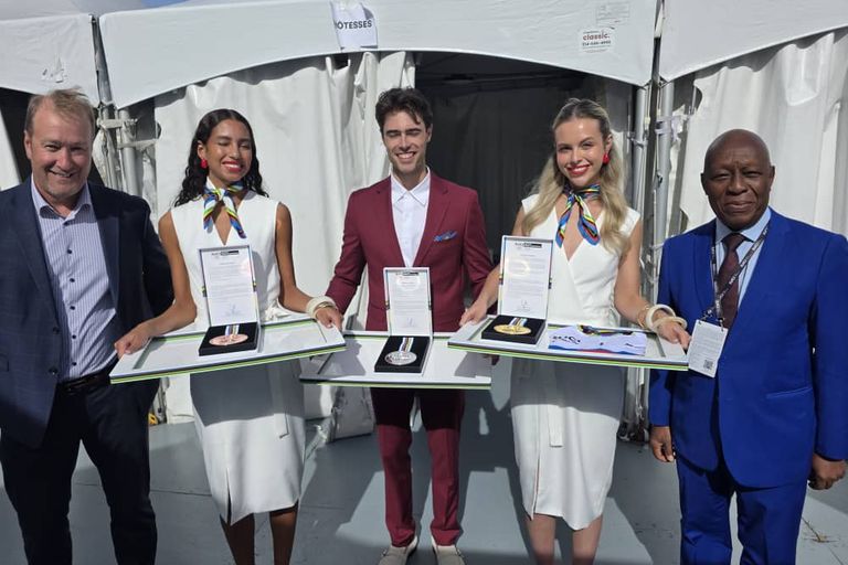 Trois plateaux portant une médaille de bronze, d'argent et d'or, tenus par des hôtes, à côté du président de la CAC