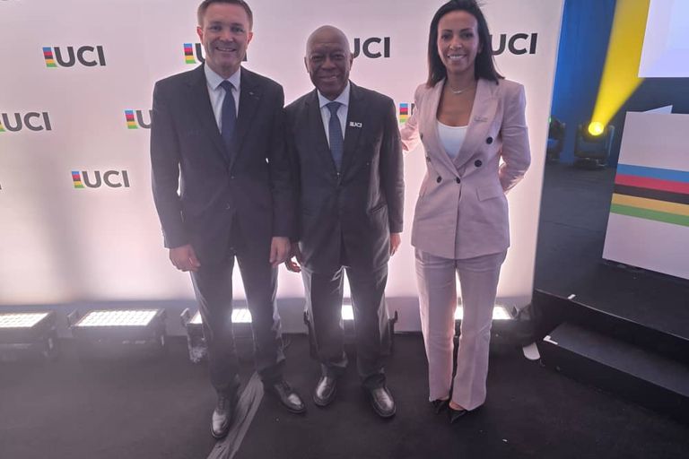 Le président de la CAC entre deux personnes, devant un mur aux logos de l'UCI