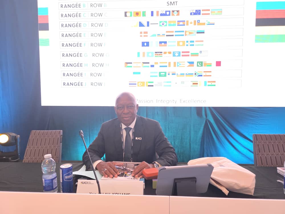 Le président de la CAC assis à sa table de séance, devant un écran qui place les délégations par rangée et par drapeau